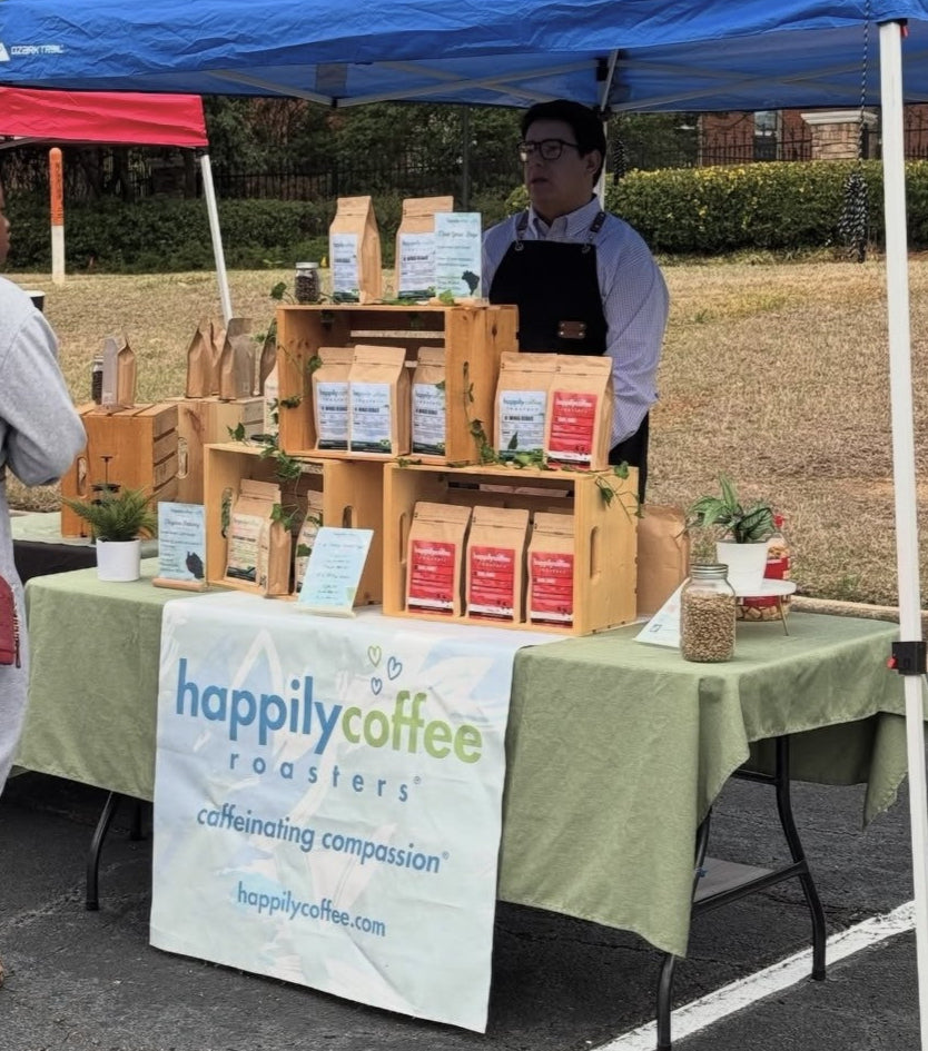 Happily Coffee Roasters booth at an outdoor event with a blue tent and coffee products on display.