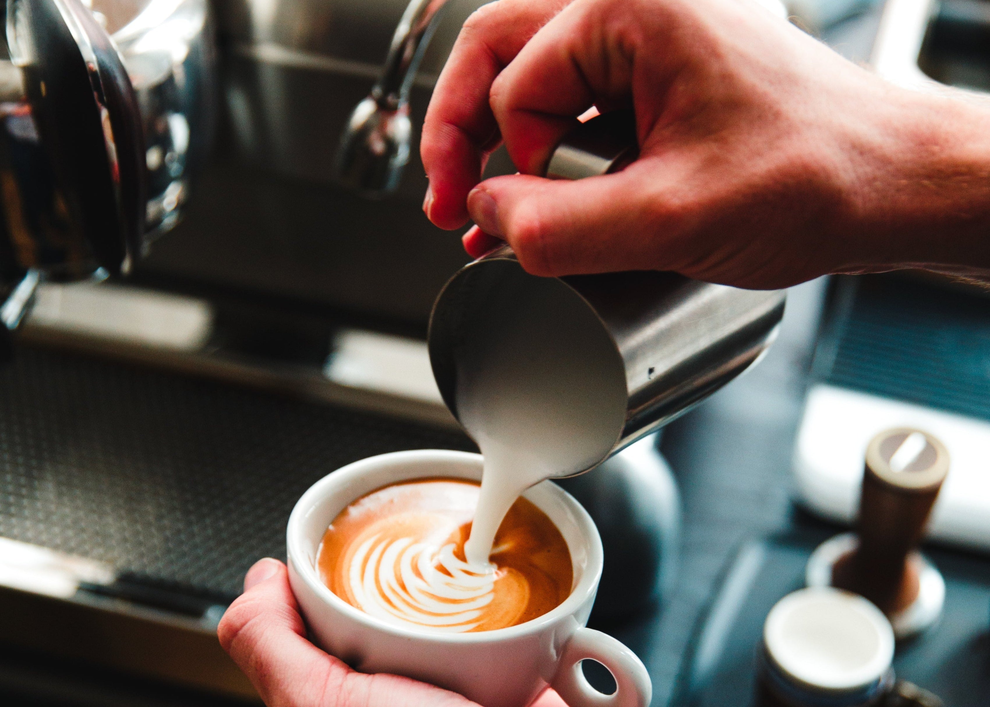 Person pouring milk into a cup of coffee with a focus on the creamy texture.